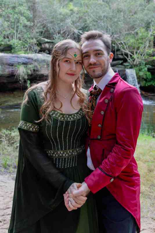 Bride and groom holding hands. Bride wears a green velvet dress and groom is in a red jacket
