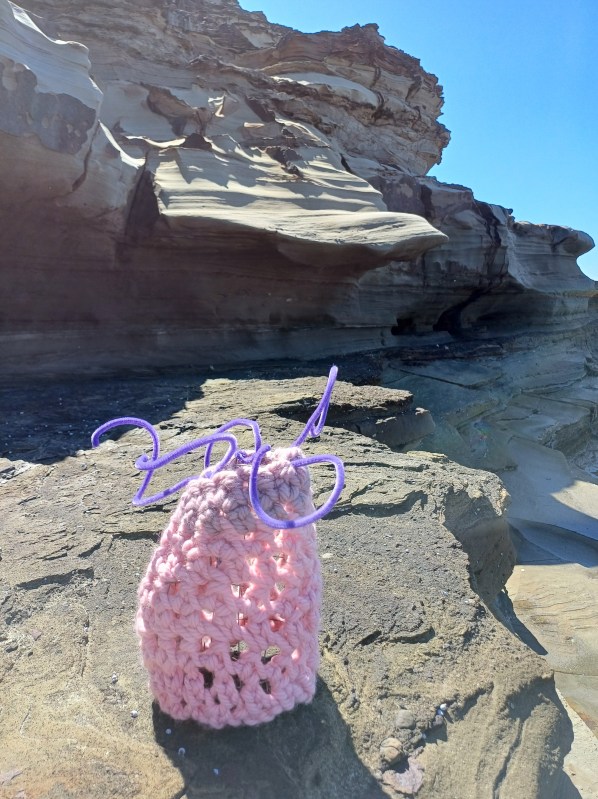 crocheted pink barnacle with purple feelers on rock shelf near beach