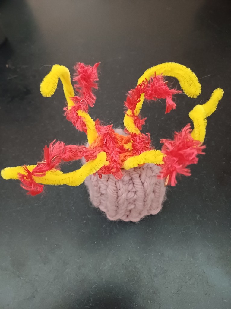 small purple knitted barnacle with yellow and red pipe-cleaner feelers, on a black background