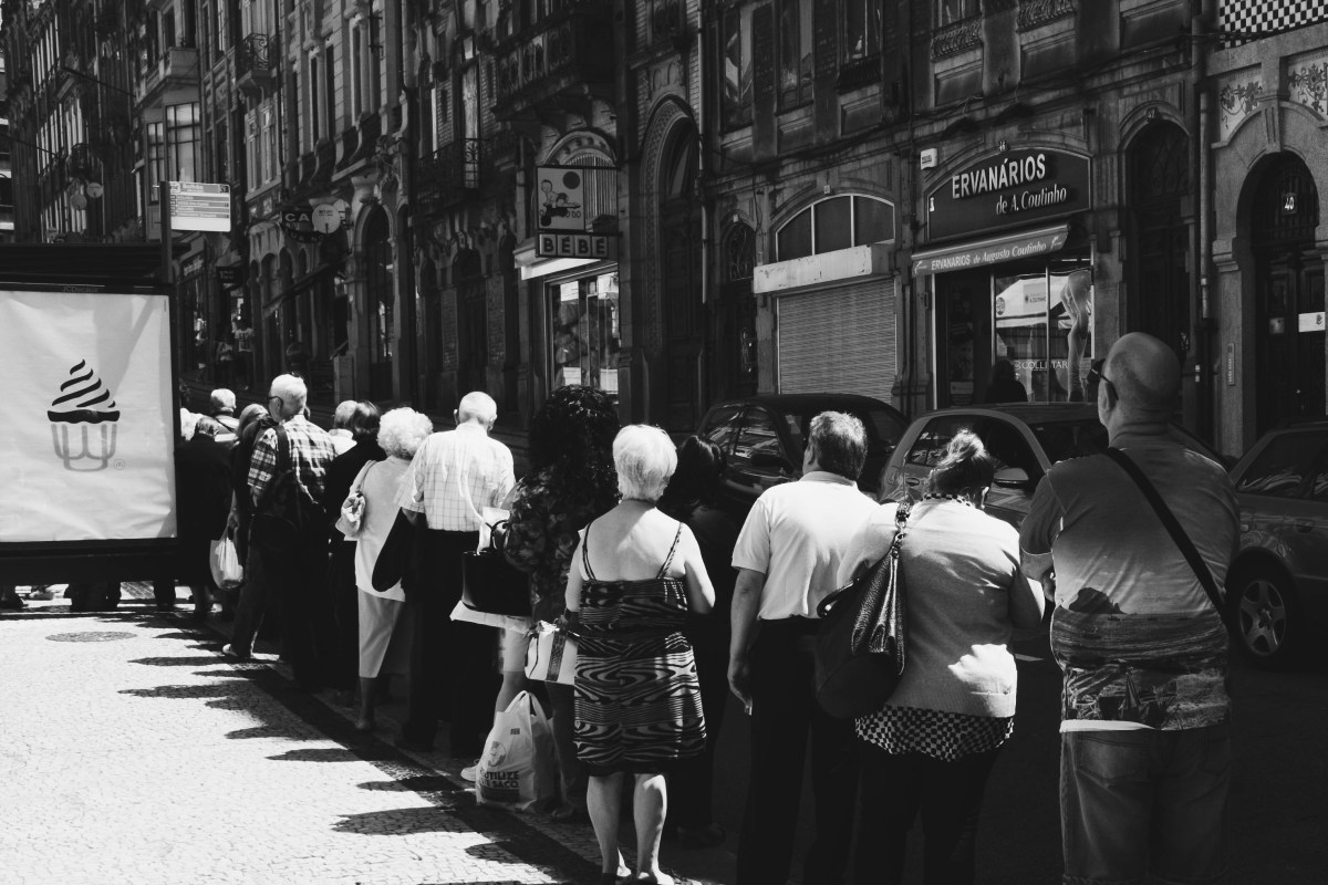 black and white image of people waiting outside in a very long queue, in a Latin country