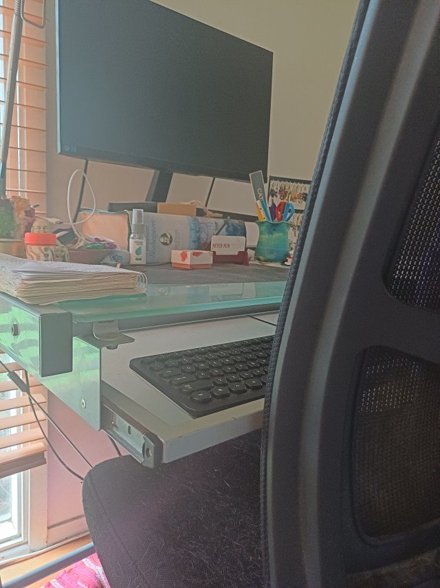 desk chair and computer desk with monitor and keyboard; desk is cluttered with other items and there is car fur on the chair seat
