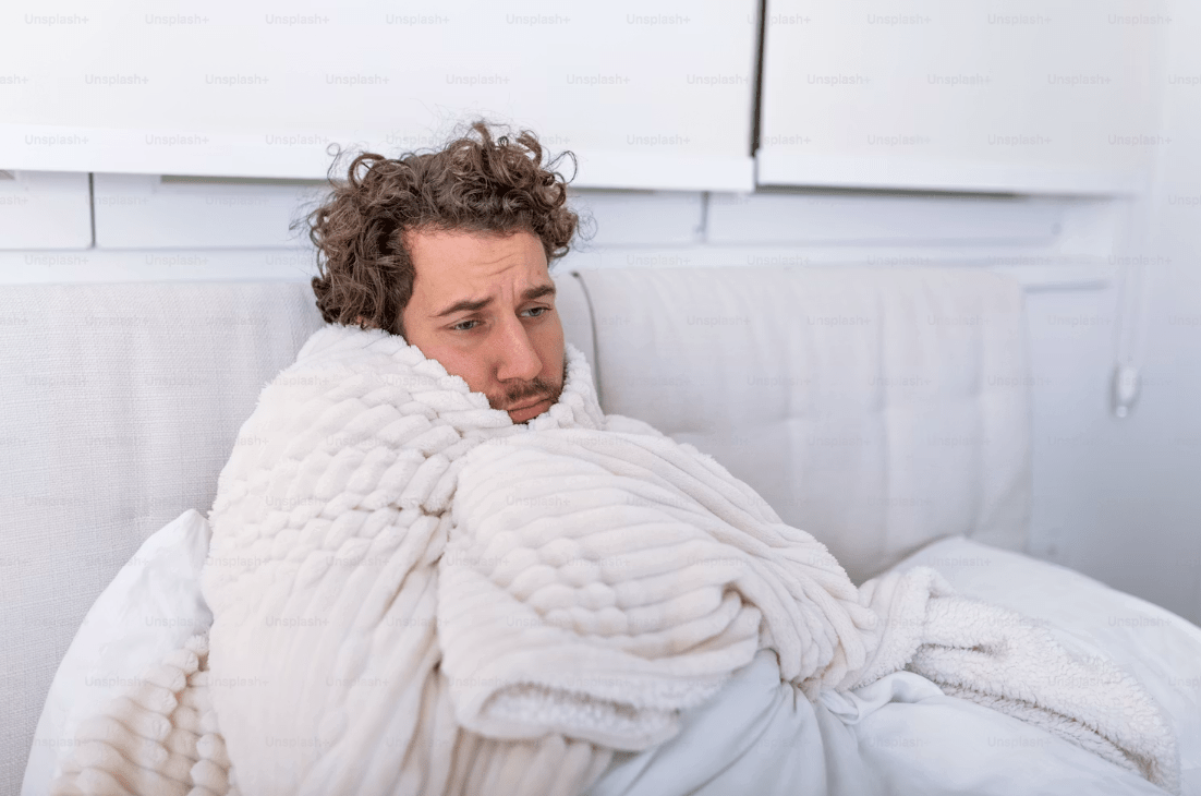 Man sitting up wrapped in a blanket looking sad and ill