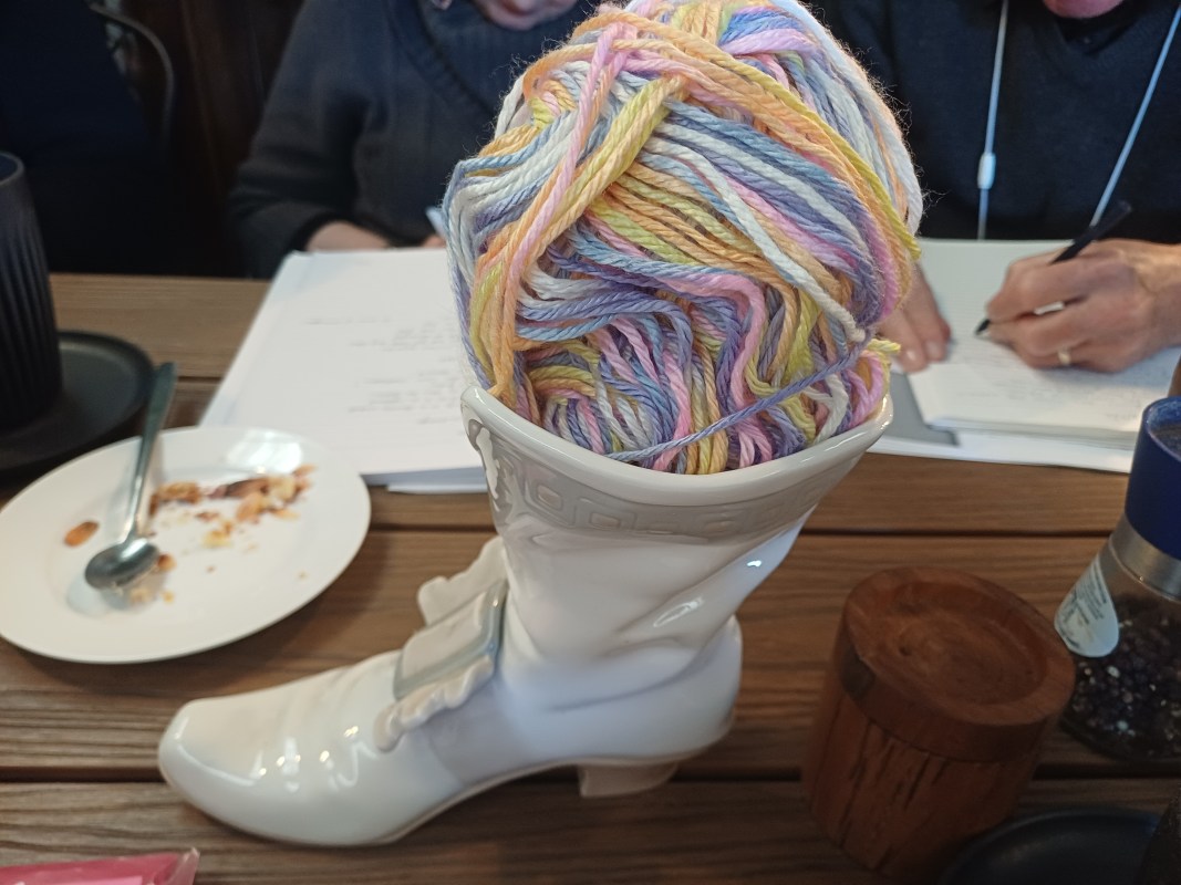 white crockery boot with a ball of rainbow yarn in the top, sitting on a cafe table